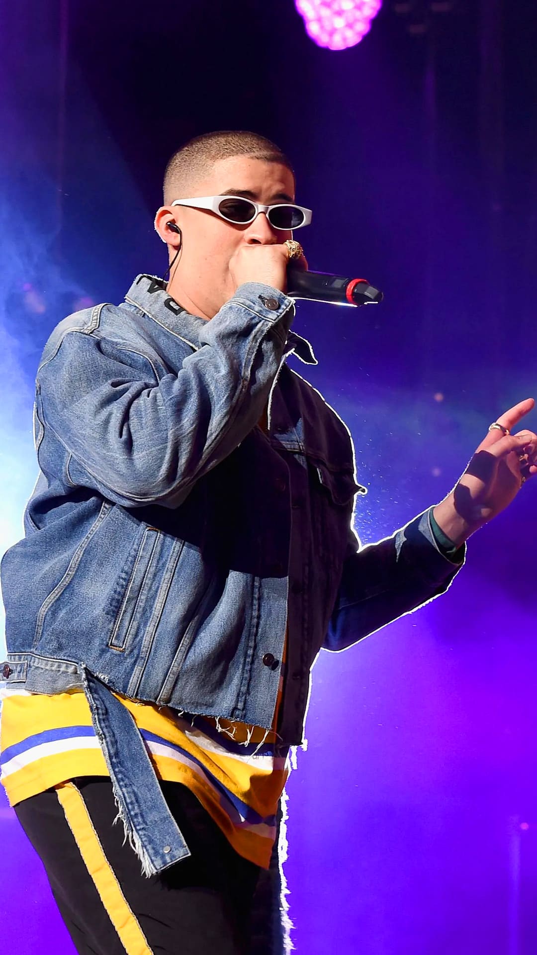 A man wearing sunglasses and holding up his microphone - Bad Bunny