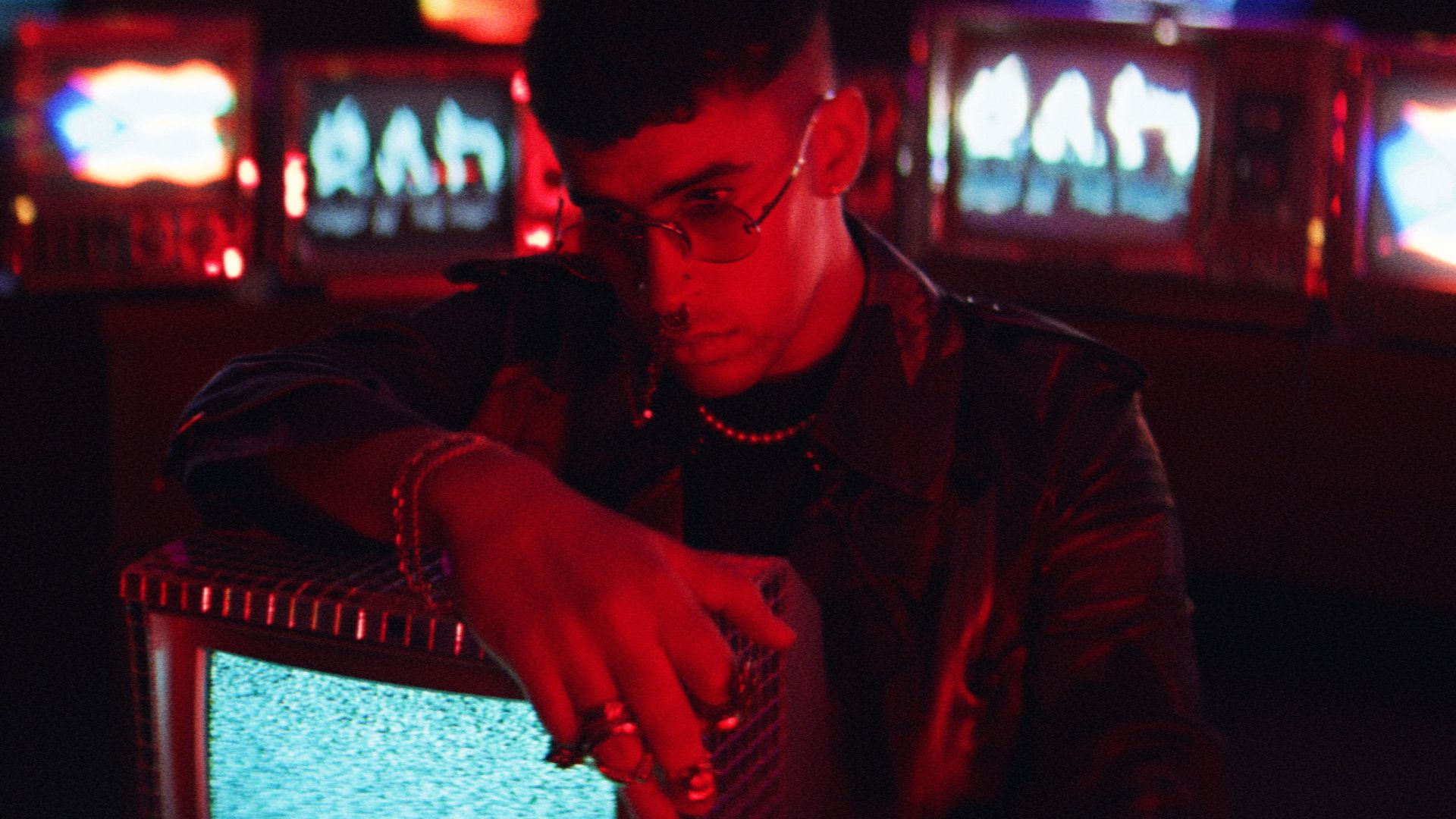 A man in leather jacket and glasses with his hand on an old tv - Bad Bunny