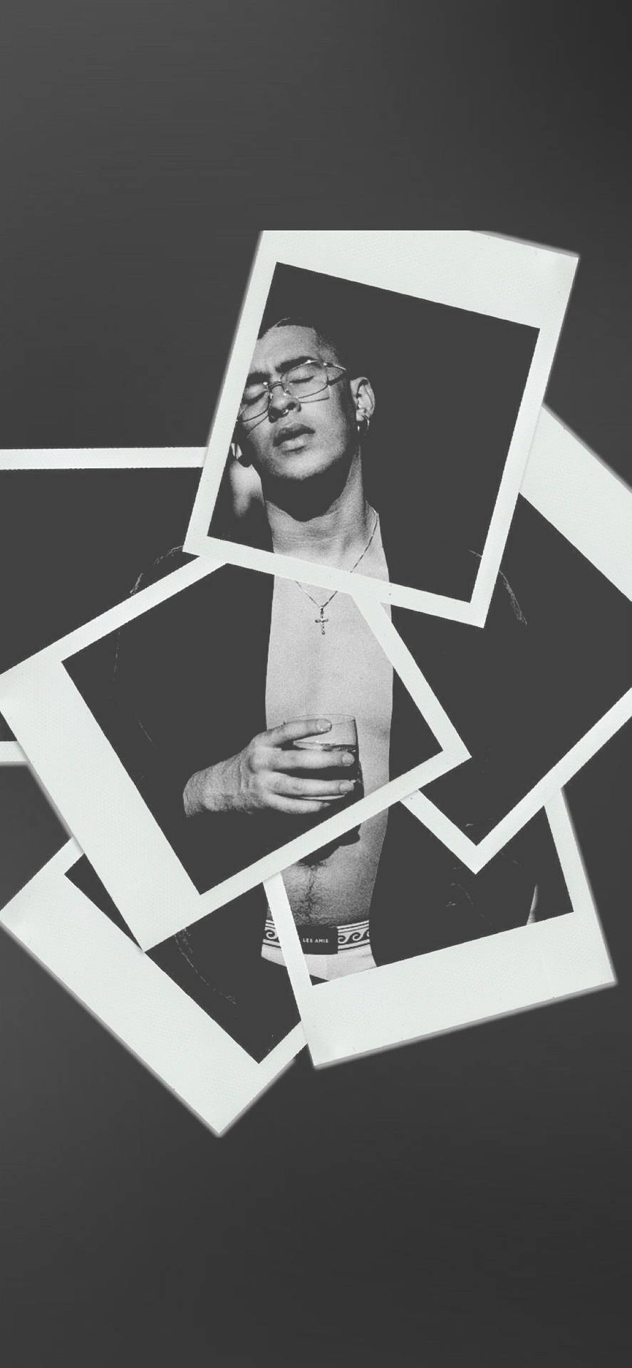 A black and white photo of a man with glasses and a white tank top. He is holding his stomach and looking to the side. There are polaroid pictures of him laid out around him. - Bad Bunny