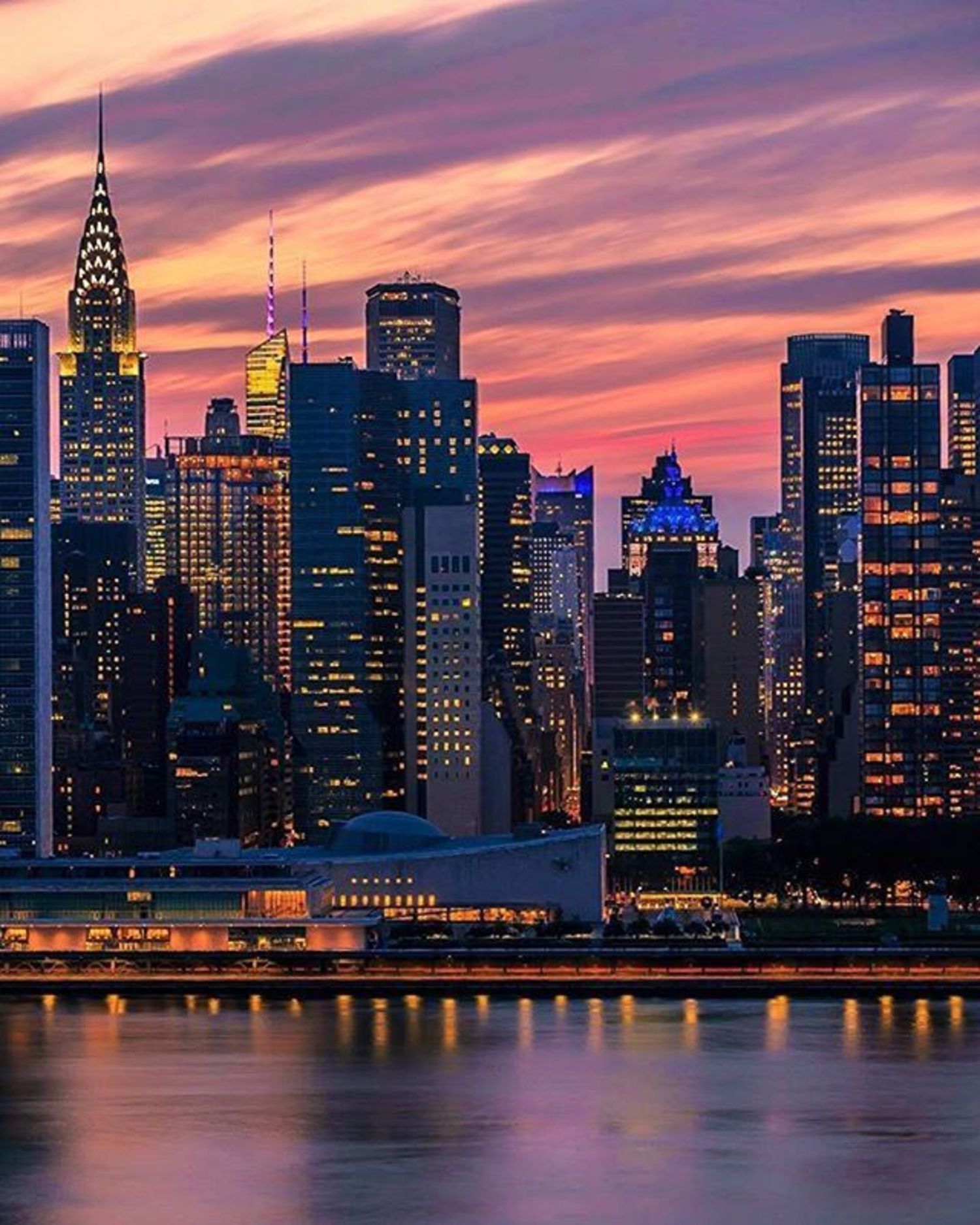 A beautiful sunset in New York City with the lights of the buildings reflecting in the water. - City, cityscape, New York