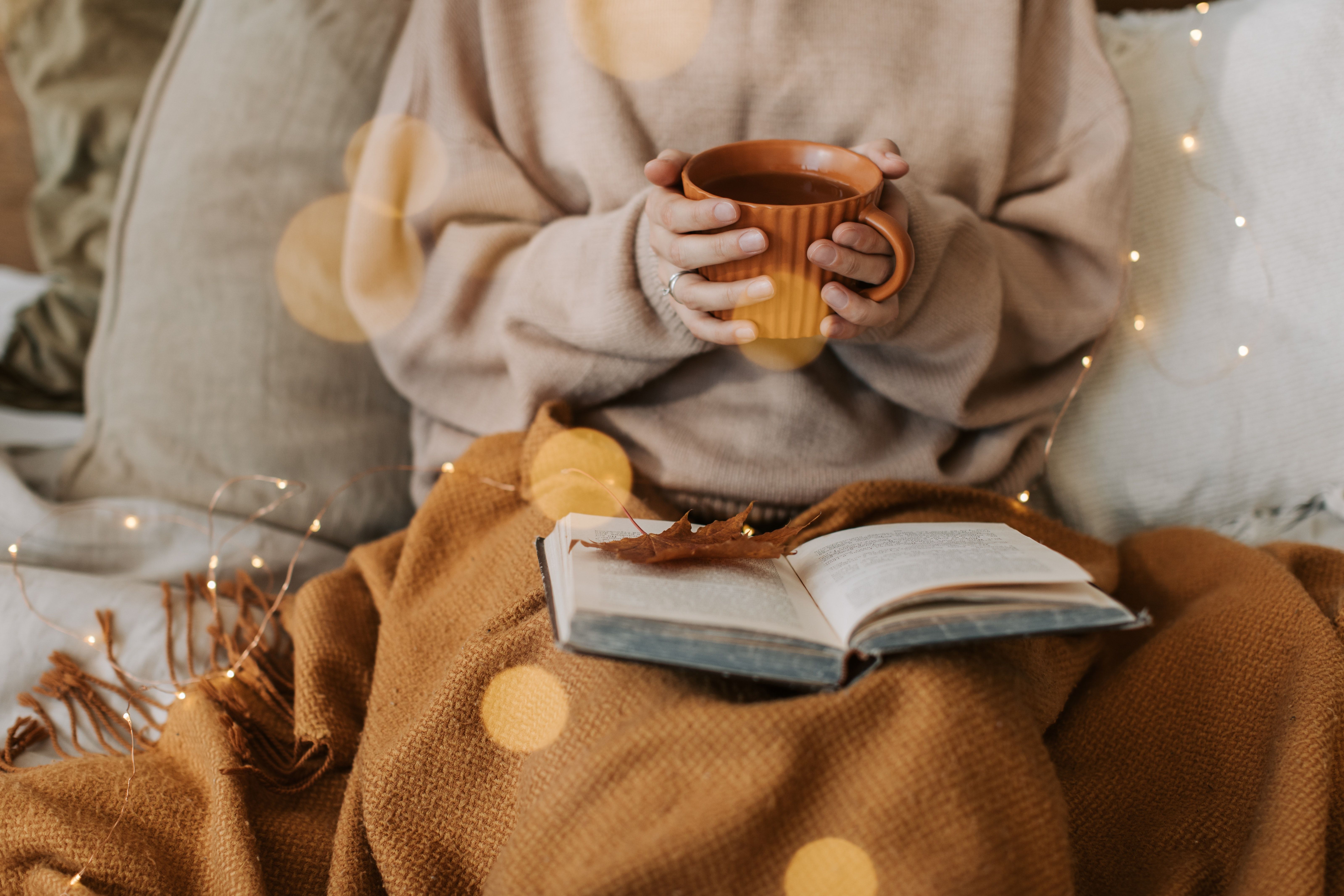A person holding a cup of tea and a book - Books