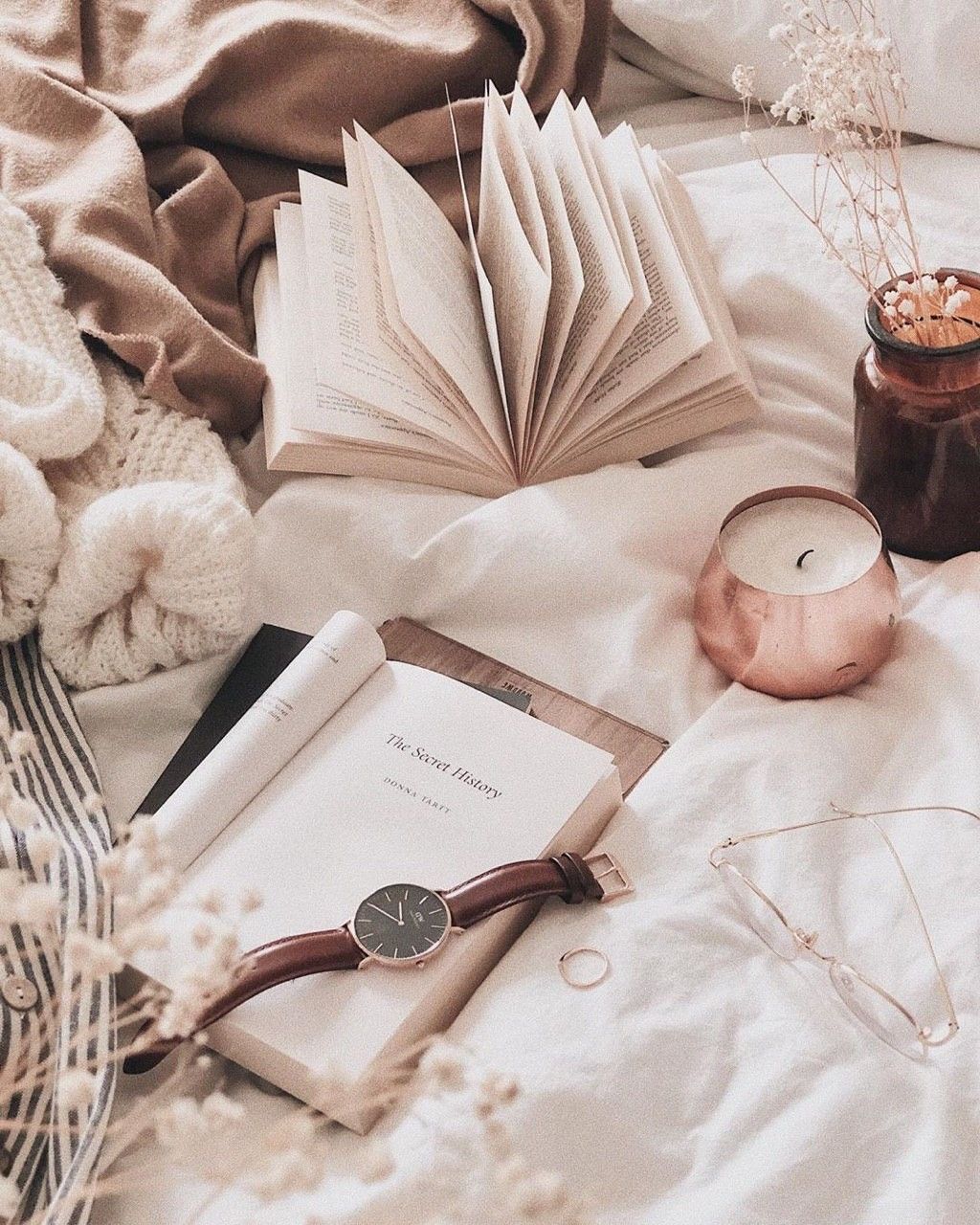A book, a watch, a candle, glasses, and a teddy bear are on a bed. - Books
