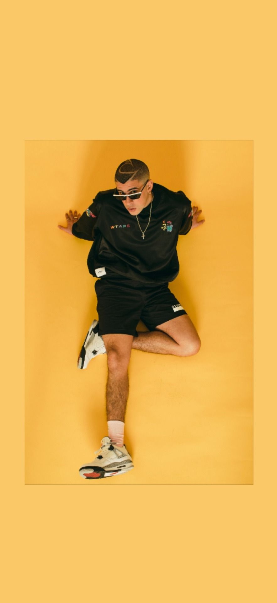 A man in black shirt and shorts standing on one leg on yellow background - Bad Bunny