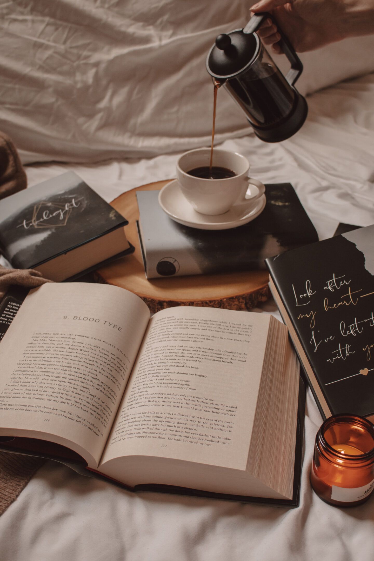 A book open on a bed with a cup of coffee being poured into a mug. - Books, coffee