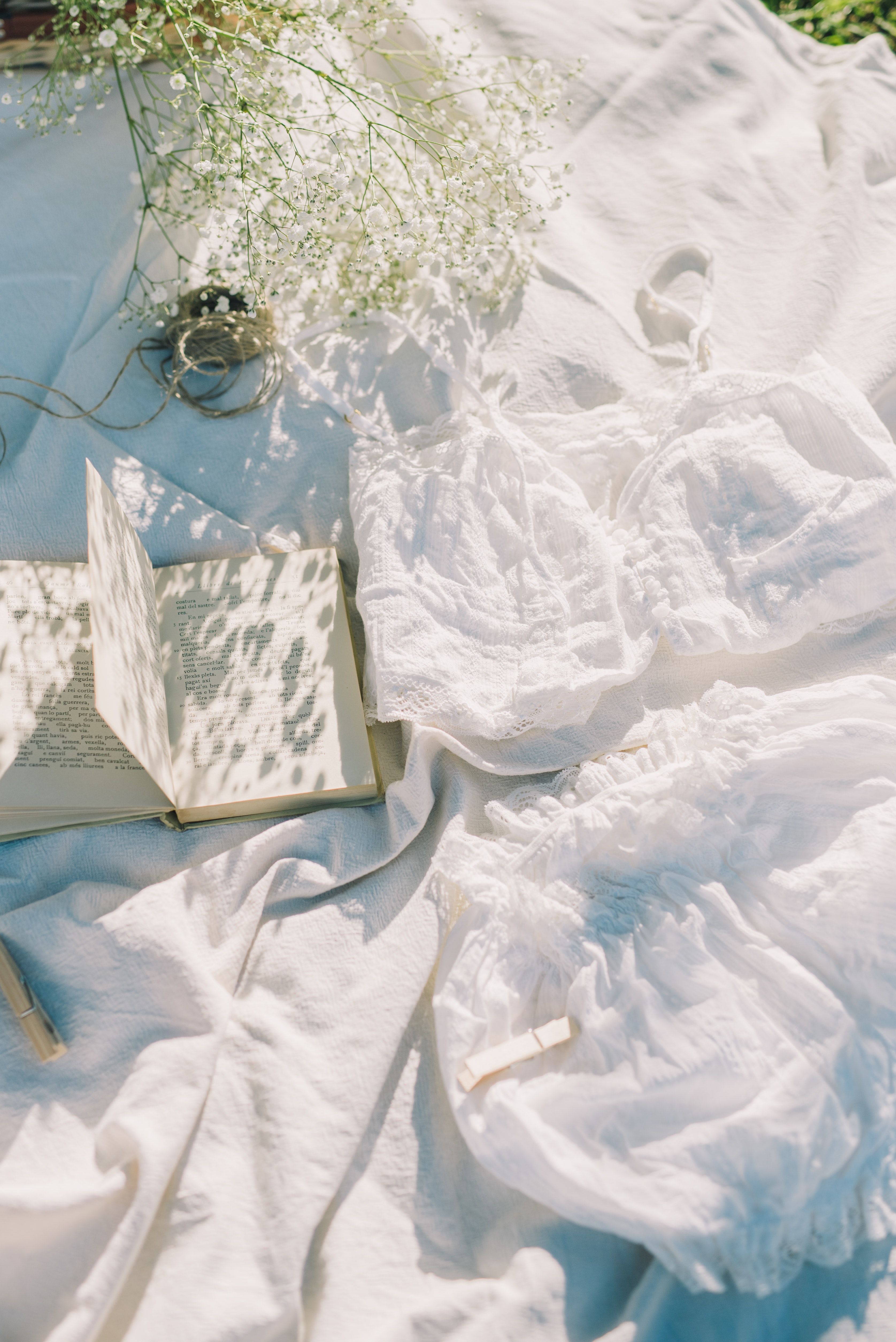 A white blanket with a book, flowers, and a dress on it. - Books, white, France, cute white