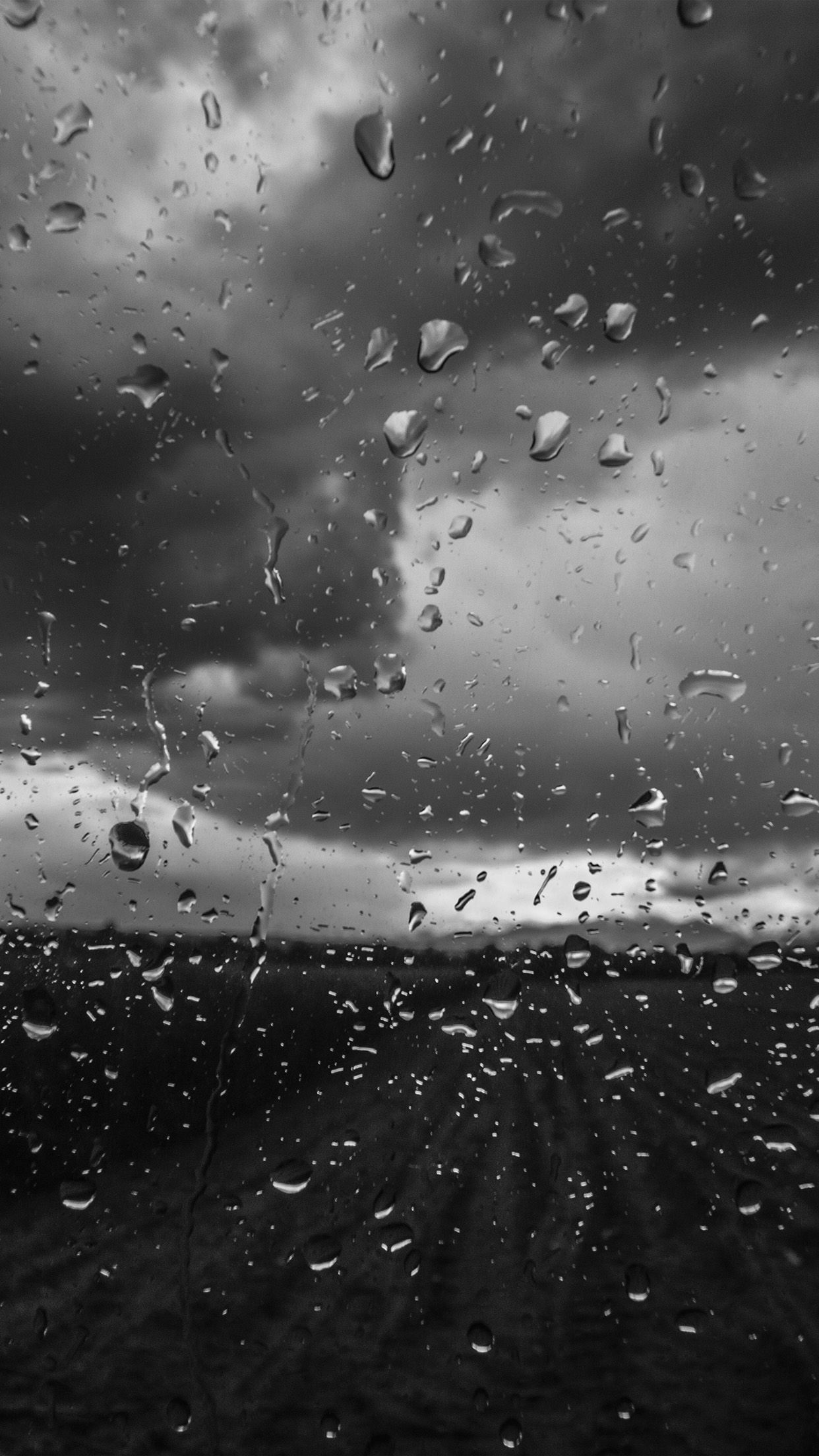 A black and white photo of a rain-streaked window with a dark sky in the background. - Rain