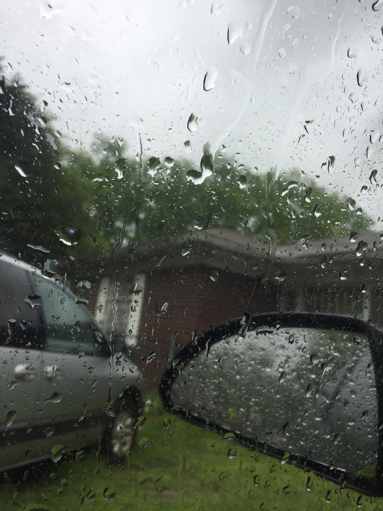 A car is parked in a driveway with rain falling on the window. - Rain