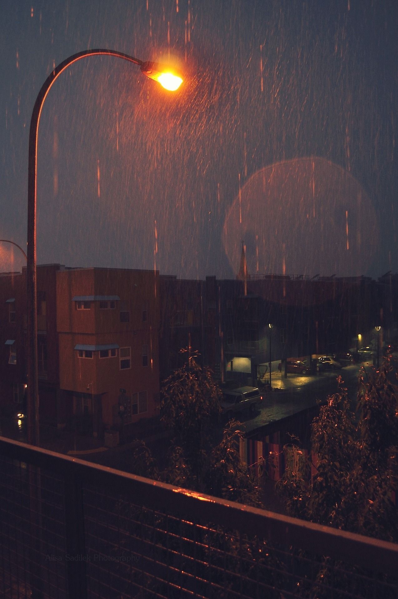 A street lamp shines in the rain, illuminating the street below. - Rain