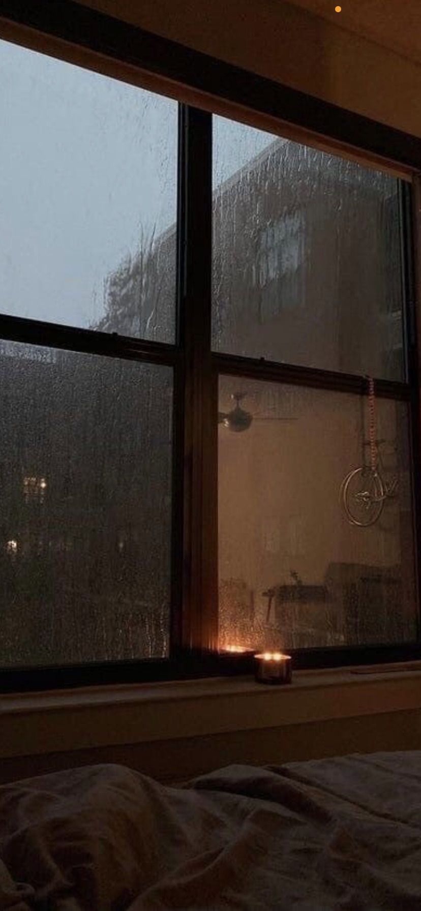 A bedroom with a candle on the windowsill - Rain