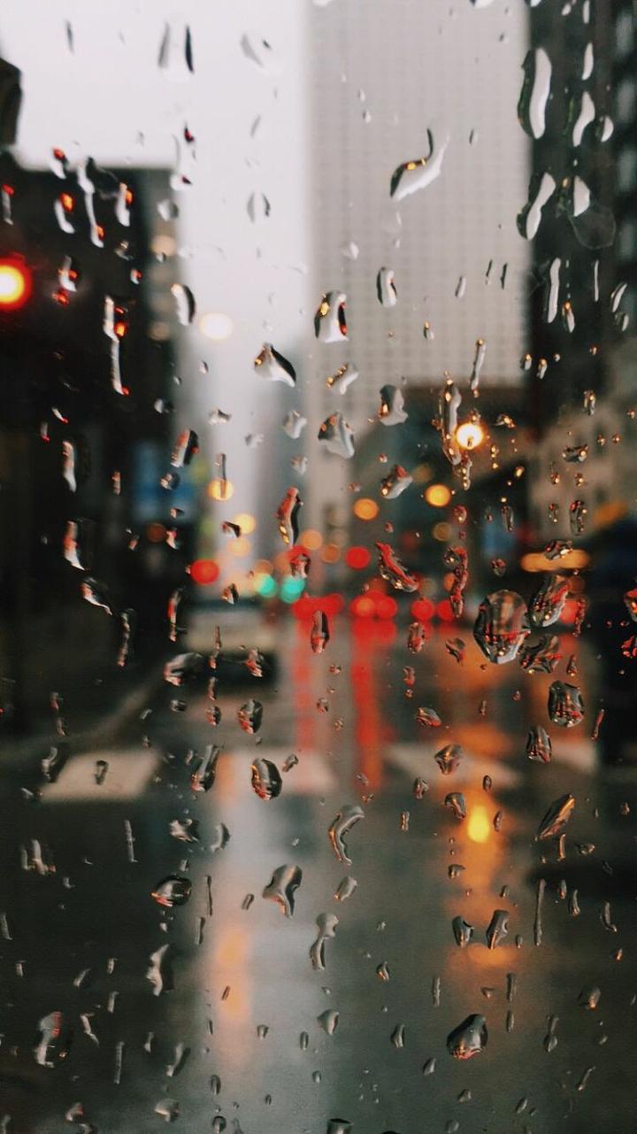Raindrops on a window, with a blurred city street in the background. - Rain